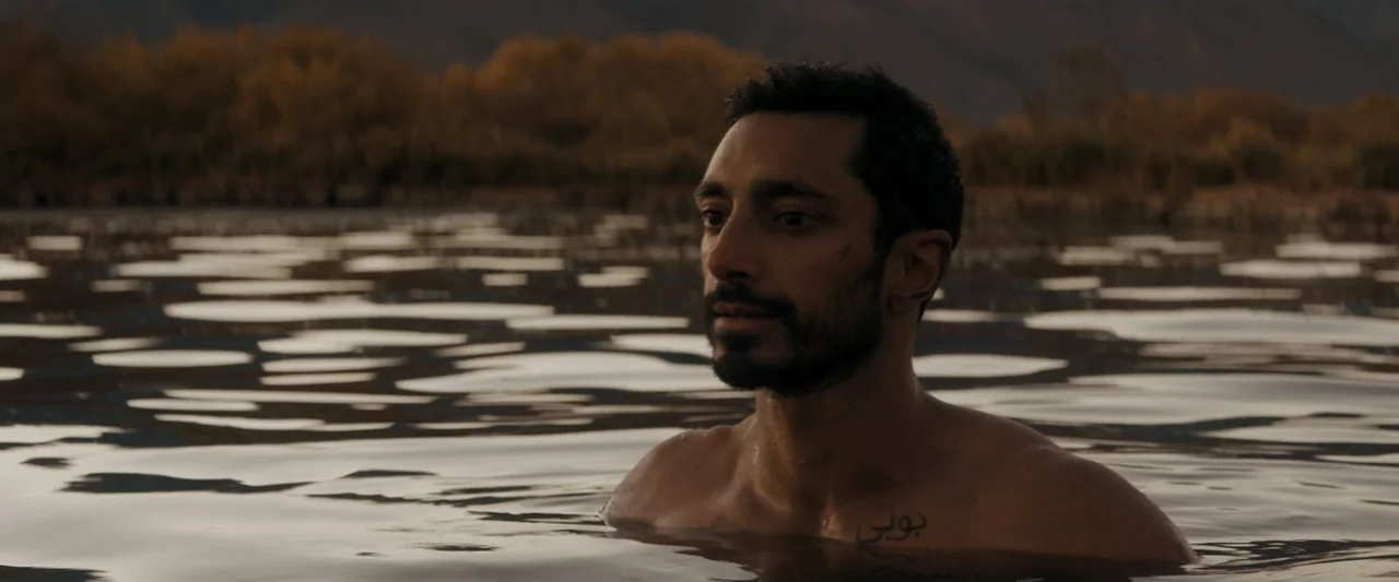 Encounter (2018) movie still: medium — A man stands in the middle of a calm lake during golden hour light. The water surface reflects the…