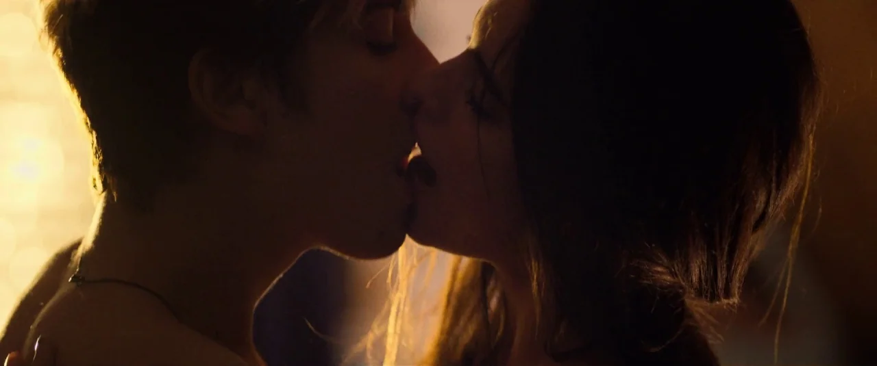 Death Note (2017) movie still: closeup — A dimly lit room provides a dark backdrop for the close-up of two people. A man and a woman press their…