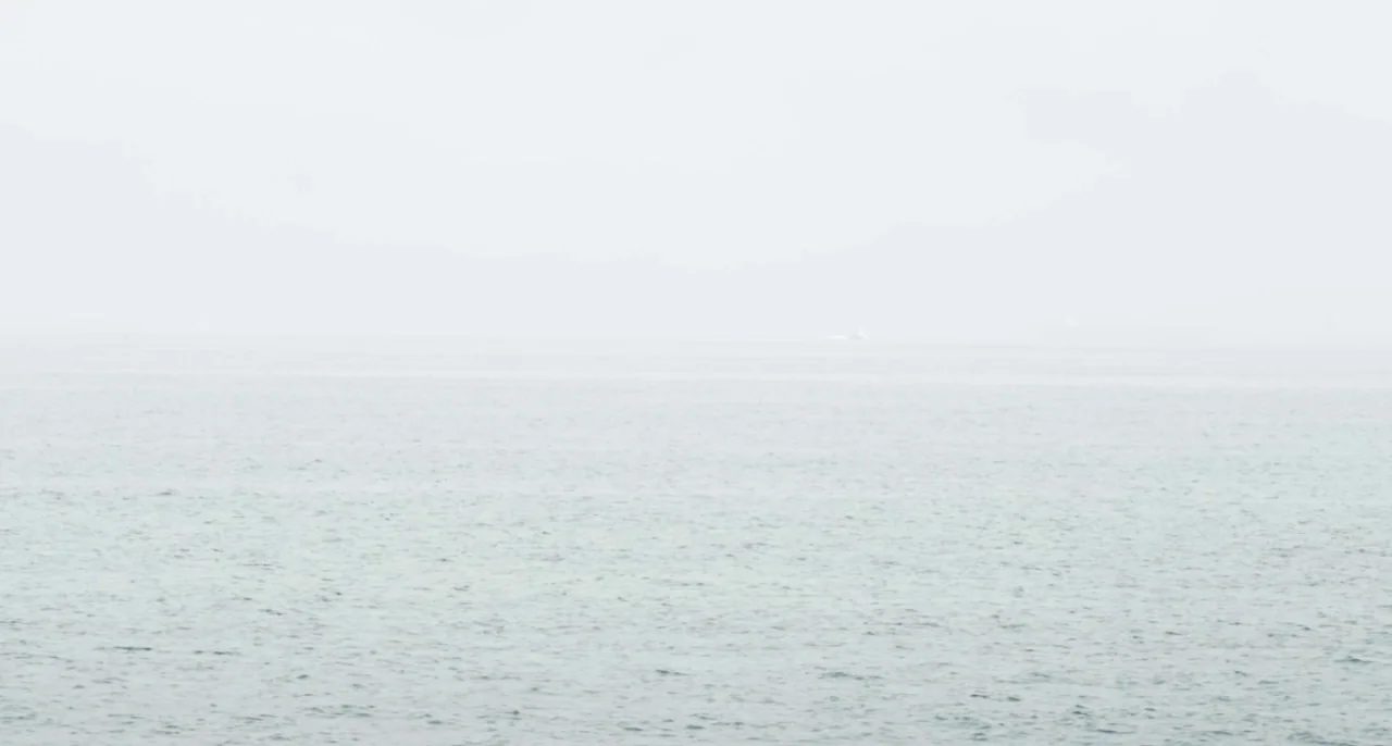 Bastards (2013) movie still: establishing — A vast, calm expanse of grey water stretches to a pale, misty horizon line. No landmarks or other…