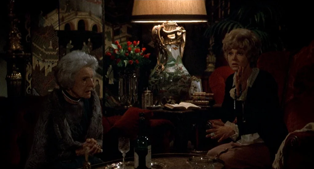 Family Plot (1976) movie still: medium — An opulent living room features velvet furniture and a decorative ceramic table lamp. Two women sit near a…