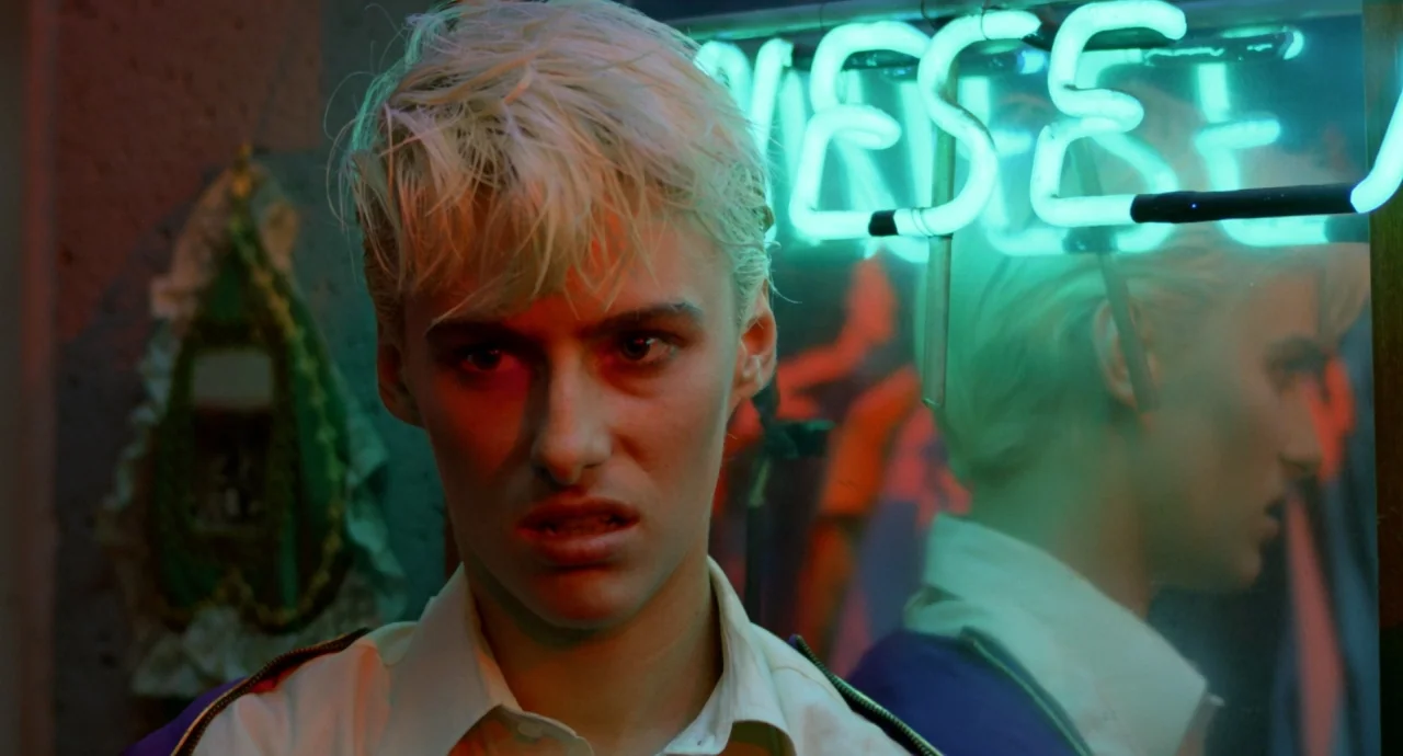 Liquid Sky (1982) movie still: closeup — A dimly lit room features a glowing neon sign reflecting in a nearby mirror. A young person with bleached…