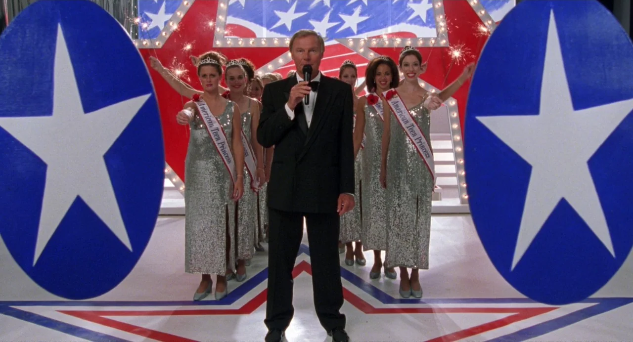 Drop Dead Gorgeous (1999) movie still: fullbody — A pageant stage features red, white, and blue star-shaped decorations and large blue ovals. A man…