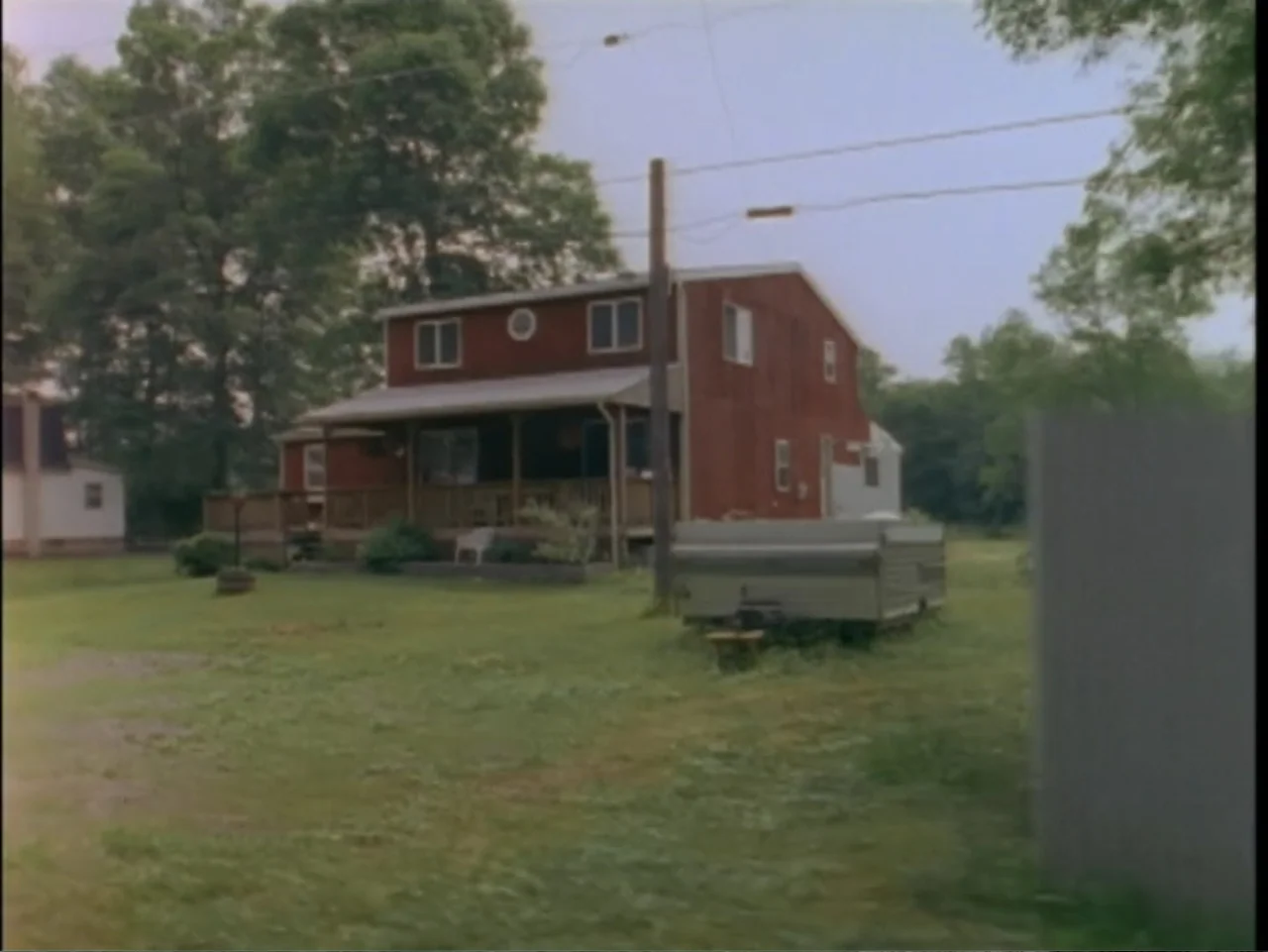 5 American Handguns - 5 American Kids (1995) movie still: establishing — A rural red house with a porch sits on a grassy lot with trees. A parked…
