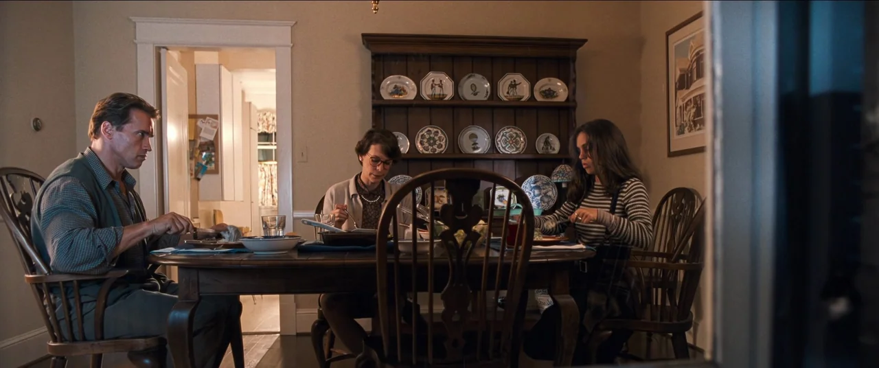 True Lies (1994) movie still: medium — A traditional dining room features a wooden hutch displaying decorative china plates. Three family members…