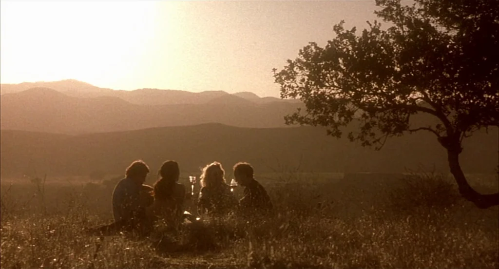 Sideways (2004) movie still: wide — A group of four friends sits on a dry, grassy hill at golden hour. Distant mountain ridges recede into a warm,…