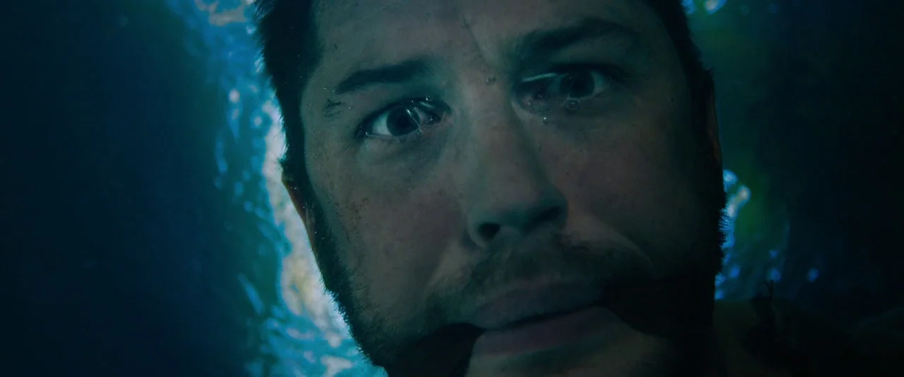 Mad Max: Fury Road (2015) movie still: closeup — A man's face is partially submerged in water, illuminated by light refracting from above. He is…