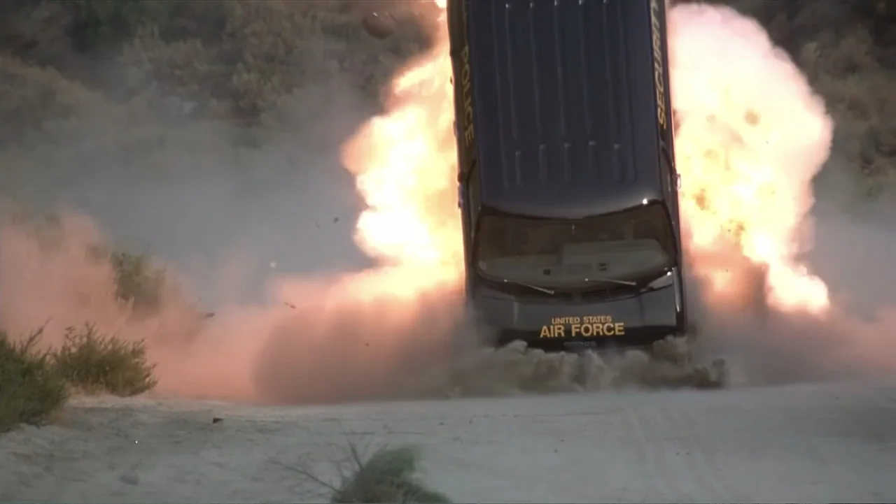 Crisis Point (2012) movie still: wide — A United States Air Force security van drives through an explosion on dirt terrain. Large clouds of smoke…