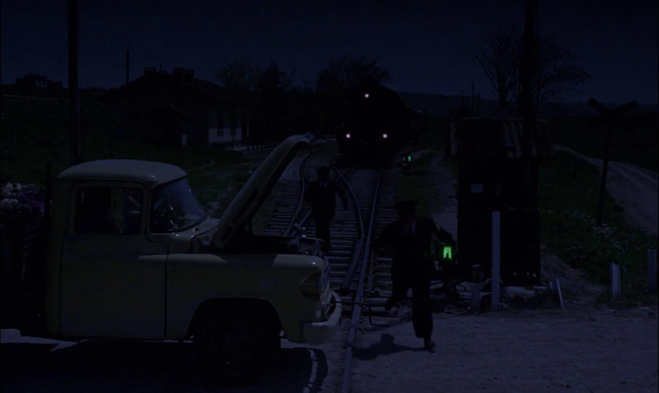 From Russia With Love (1963) movie still: wide — A rural railroad crossing at night with a stationary truck and a train approaching. Two men in dark…