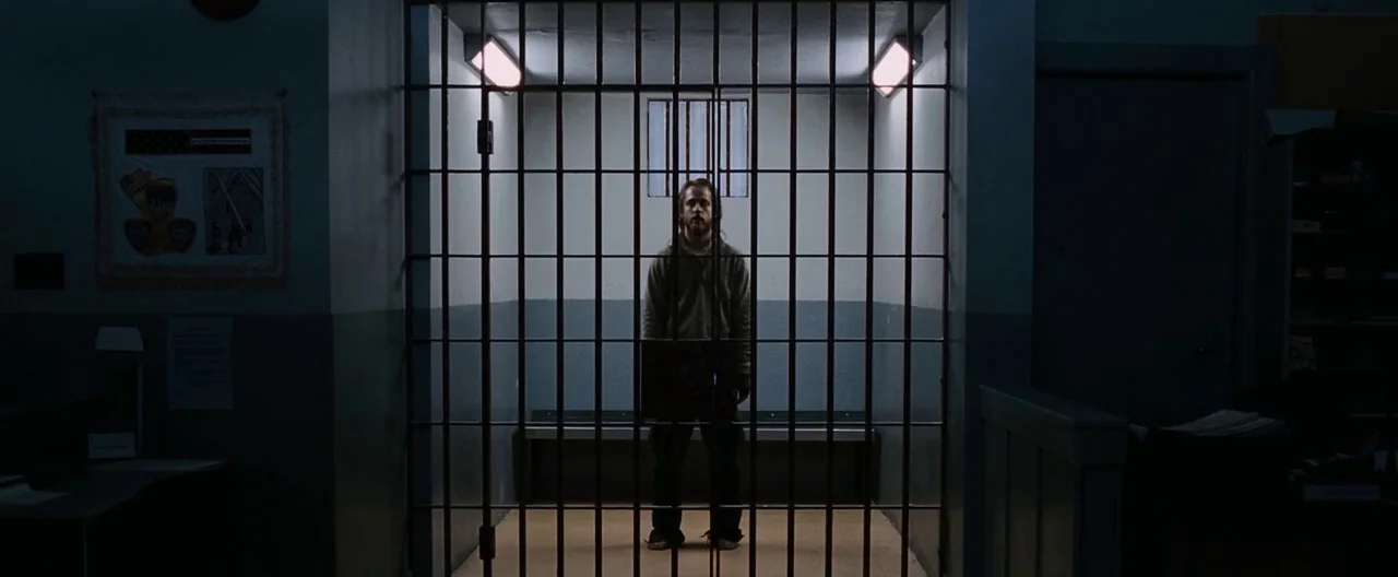 30 Days of Night (2007) movie still: medium — A small, dimly lit, secure holding area featuring vertical metal bars. A single man stands behind the…