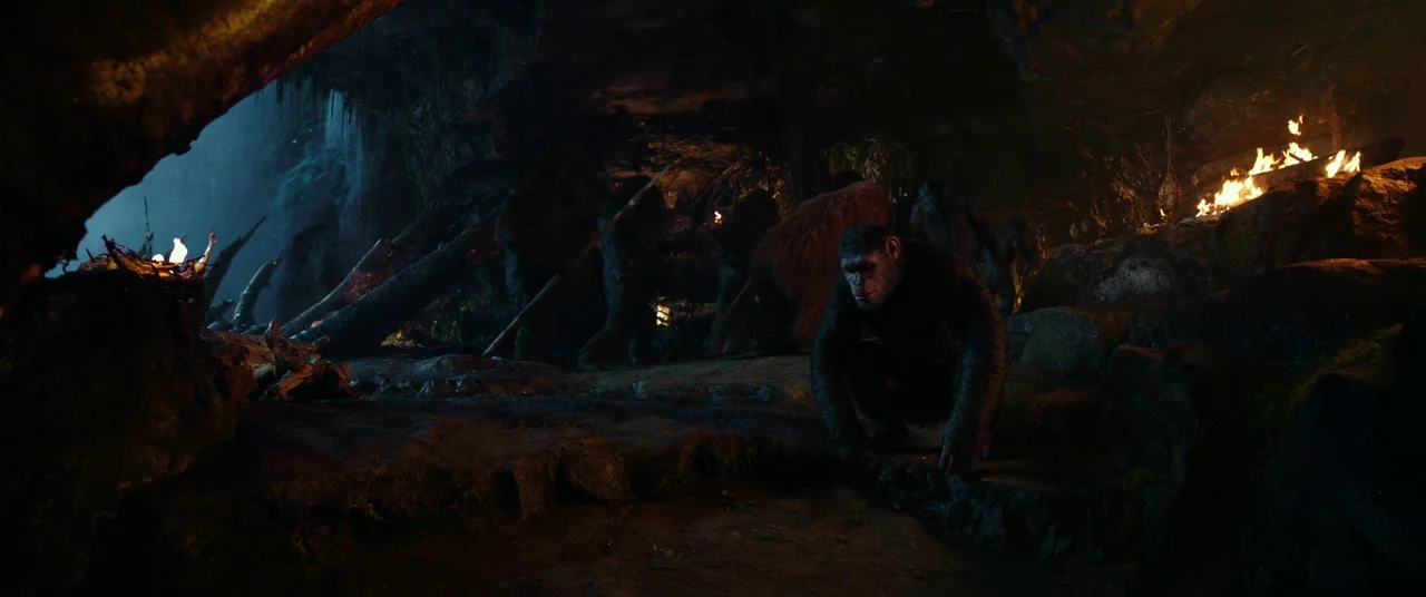 War for the Planet of the Apes (2017) movie still: wide — A dark rocky cave features a small group of chimpanzees gathering near fires. One central…