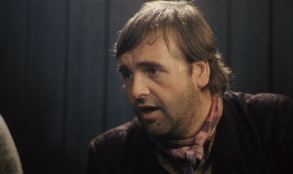 Black Jack (1979) movie still: closeup — A man stands in a dark room with vertical wooden panels visible behind him. The man looks toward the left…