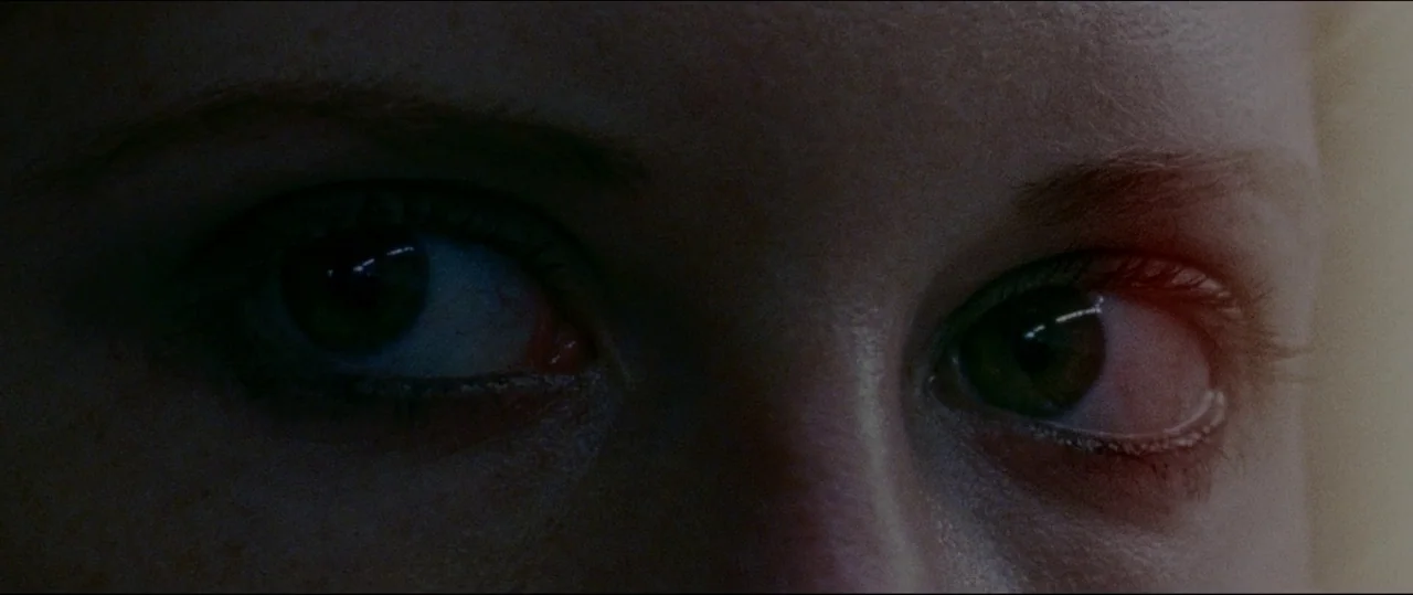 Luz (2018) movie still: closeup — A close-up view focuses on the eyes of a pale-skinned subject in darkness. The pupils are centered and look…