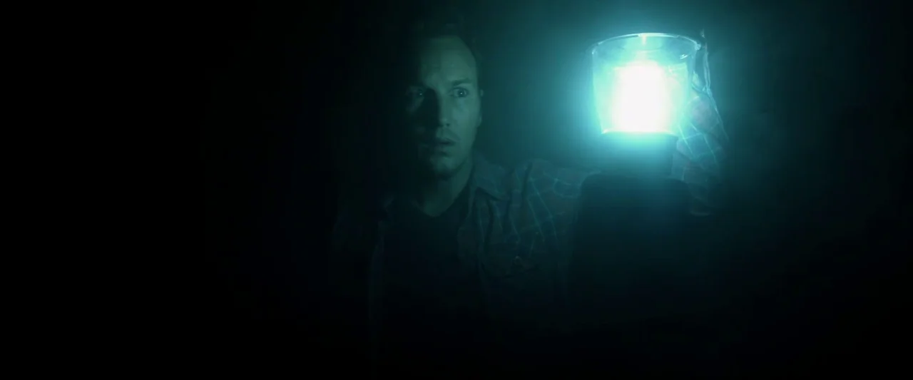 Insidious (2010) movie still: medium — A dark, undifferentiated space is illuminated only by a small handheld lantern. A man stares forward with…