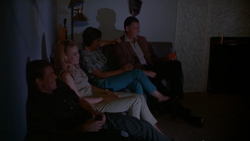 Targets (1968) movie still: medium — A dimly lit residential living room features a sofa with four people seated together. The group watches a…