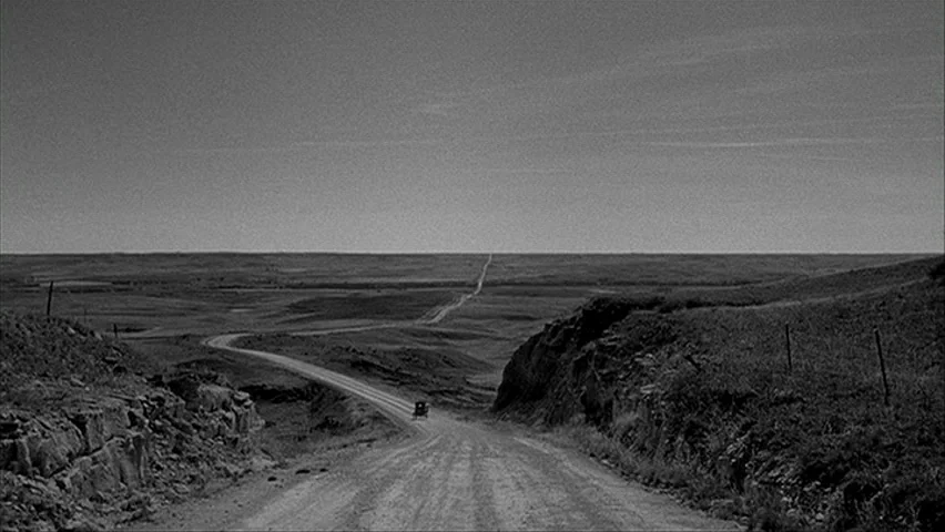 Paper Moon (1971) movie still: establishing — A vast, rolling plain stretches out under a wide, empty sky. A single dirt path cuts through the…