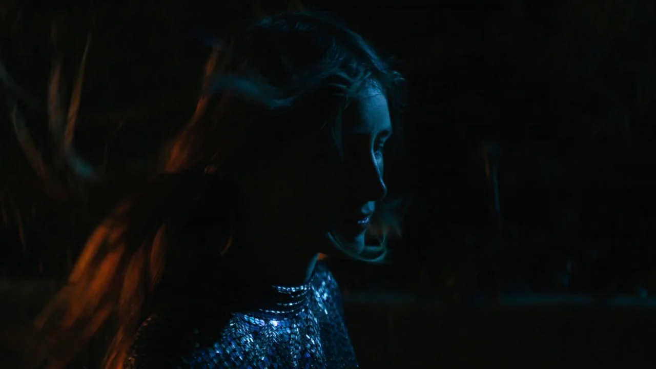 She Dies Tomorrow (2020) movie still: closeup — A woman stands in a dark space with hair blowing across her profile. Blue rim lighting highlights…
