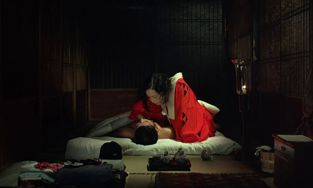 In The Realm of the Senses (1976) movie still: medium — A dimly lit traditional room features tatami mats and sliding paper walls in deep shadow. A…