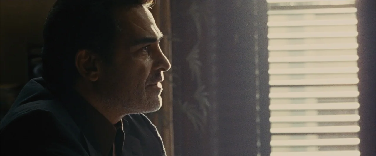 Argo (2012) movie still: closeup — A darkened interior room with sunlight filtering through closed horizontal window blinds. A middle-aged man with…