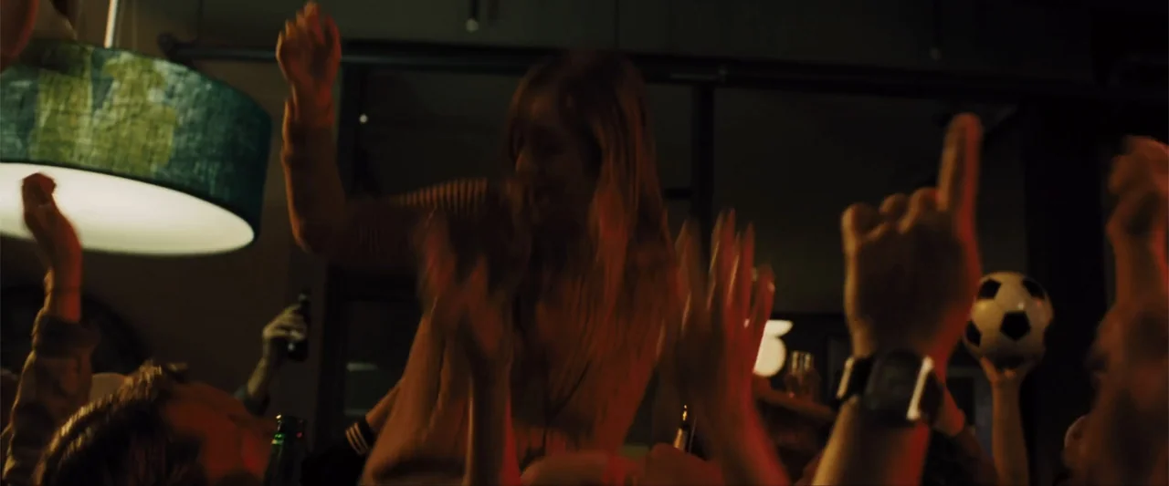 Unfinished Business (2015) movie still: medium — A dimly lit indoor gathering with people cheering and raising their hands. A woman in the center…