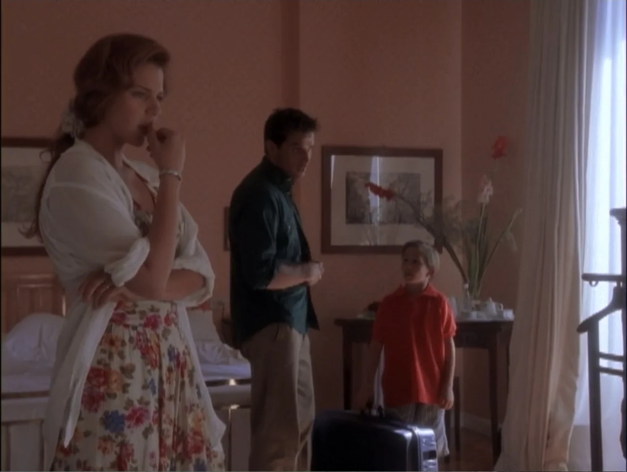 Code Name: Wolverine (1996) movie still: fullbody — A classic hotel room features peach-colored walls and a wooden console table. An adult woman, an…