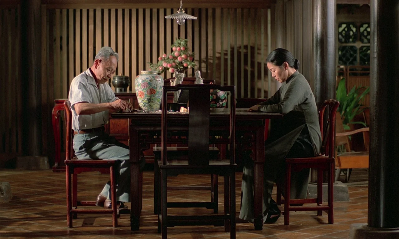 The Scent of Green Papaya (1993) movie still: wide — A traditional dining area features a large dark wooden table and slatted wood walls. An older…