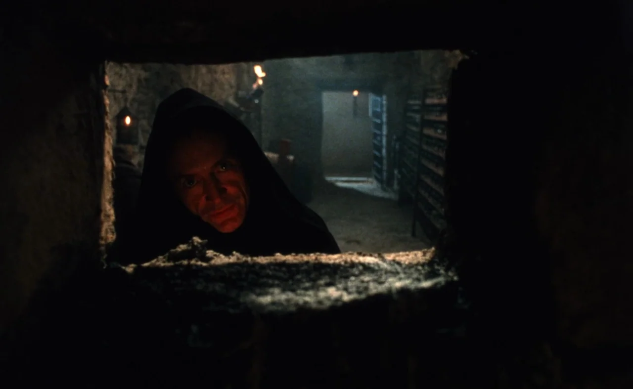 The Pit and The Pendulum (1991) movie still: medium — A dark, textured stone chamber is framed by a narrow, rectangular opening in the wall. A man…
