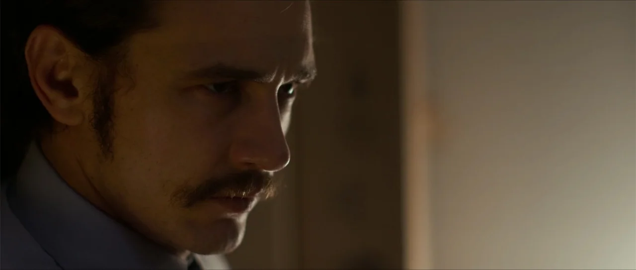 The Vault (2017) movie still: closeup — An interior space is dimly lit by a soft light source from the side. A man with a mustache looks off-camera…