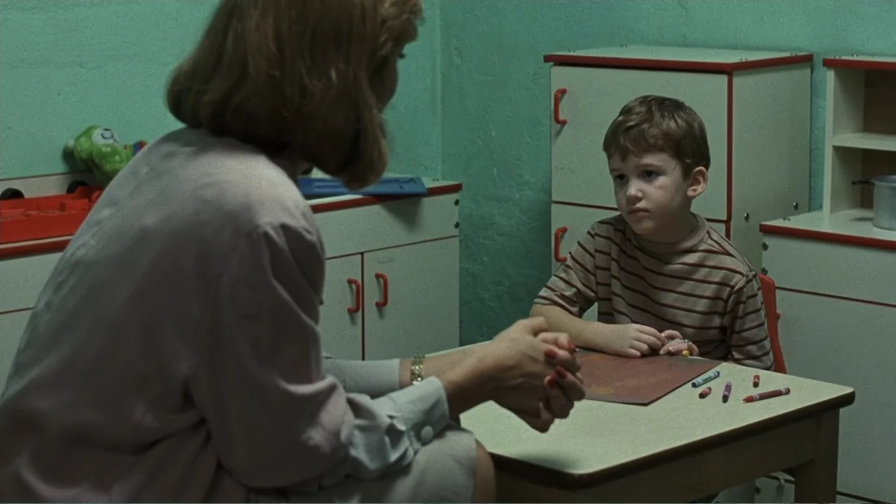 Presumed Innocent (1990) movie still: medium — An interior space with pale green walls and white toy storage units with red trim. A young boy in a…
