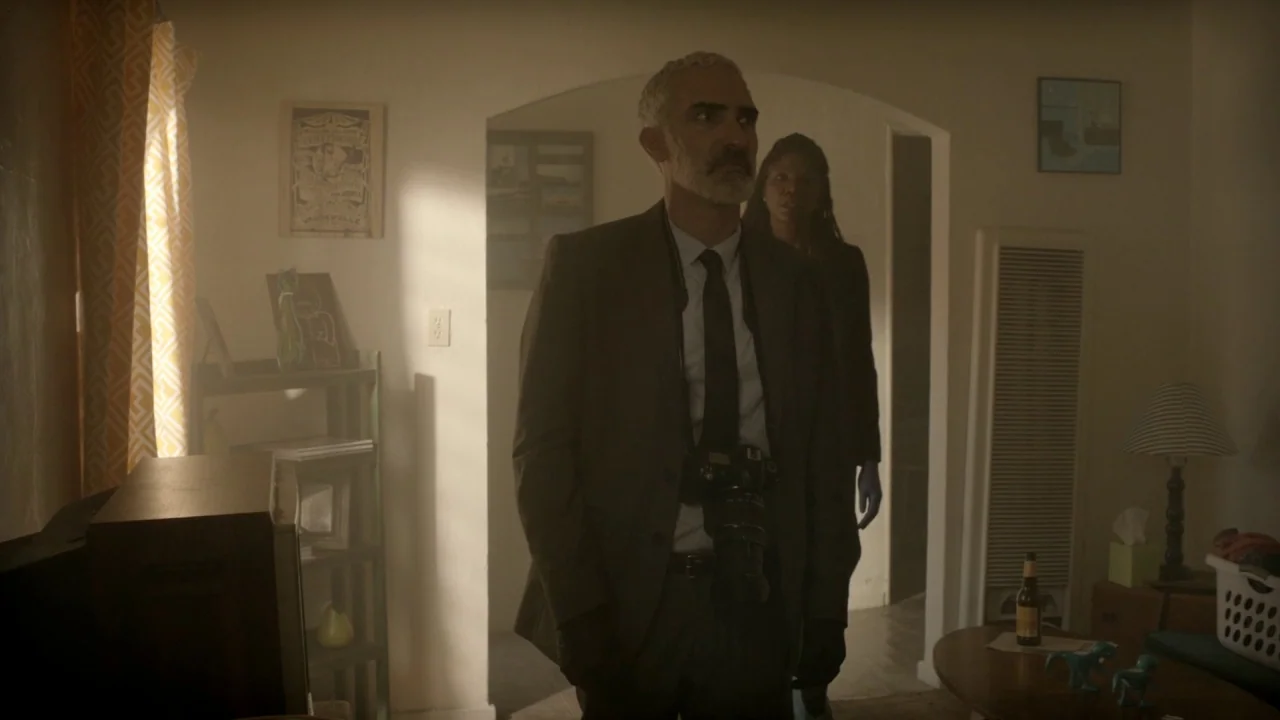 The Pact II movie still: medium — A living room interior features a white wall with an arched doorway and dust motes. A man in a suit wearing a…