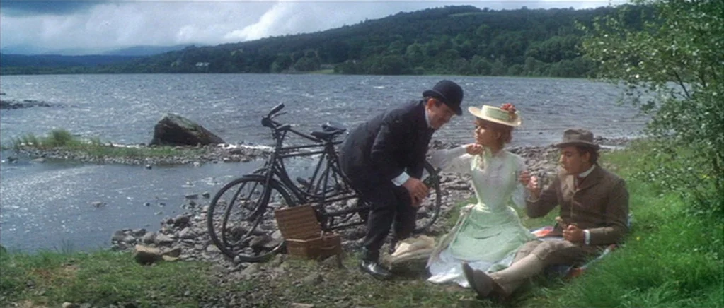 The Private Life of Sherlock Holmes movie still: wide — A lakeshore landscape with rocky terrain and green grass borders a large body of water.…