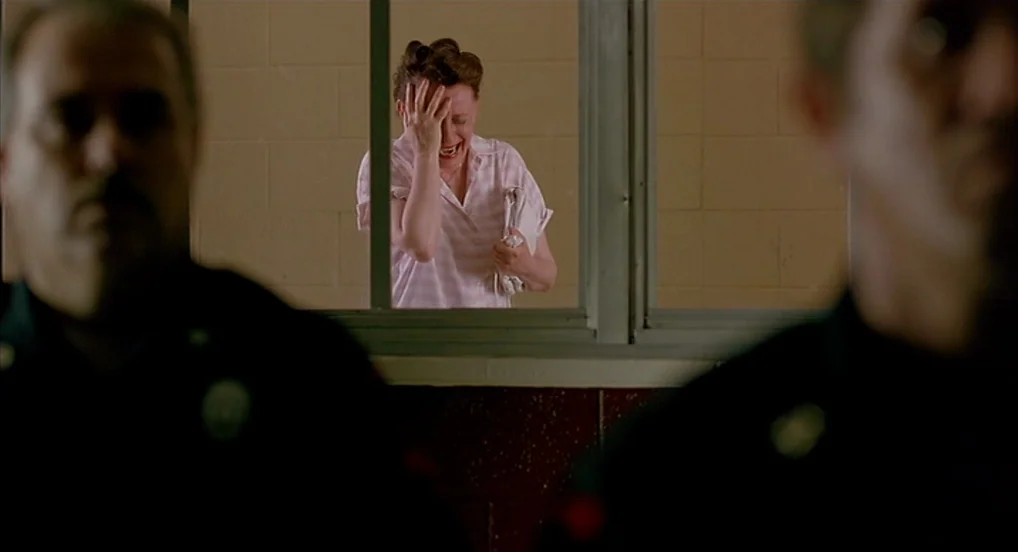 Dead Man Walking (1995) movie still: medium — A visitation room features a gray glass window panel dividing the space. A weeping woman stands in the…