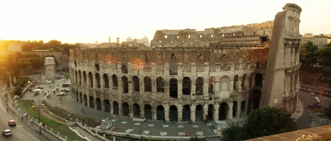 The Great Beauty (2013) movie still: establishing — The massive weathered stone facade of the Colosseum dominates the wide panoramic view at dusk. A…