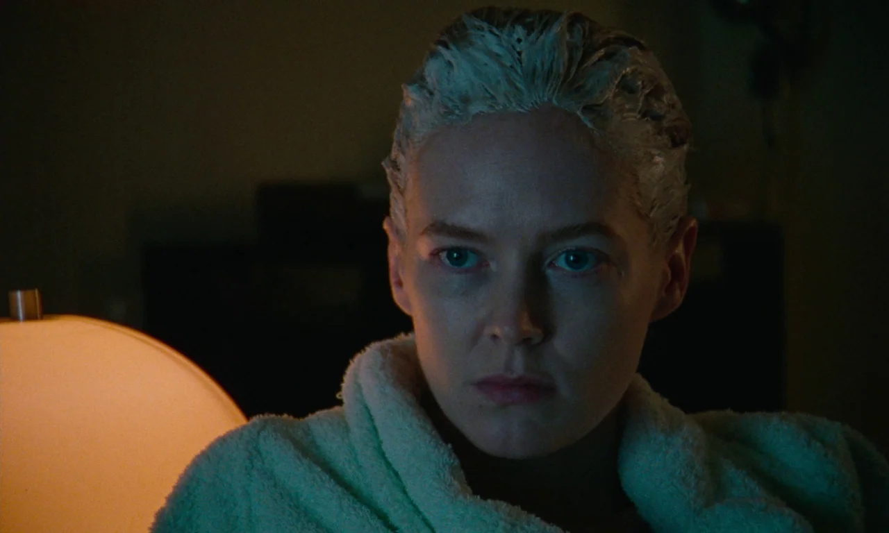 Blue Jean (2022) movie still: closeup — A dark bathroom at night with a single warm table lamp nearby. A woman wears a hair mask while staring…