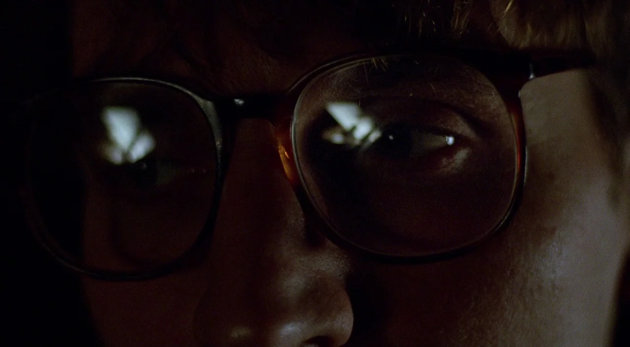 Shallow Grave (1994) movie still: closeup — A close-up shot focuses on a young man's face and eyeglasses in deep shadow. Reflections of a bright,…