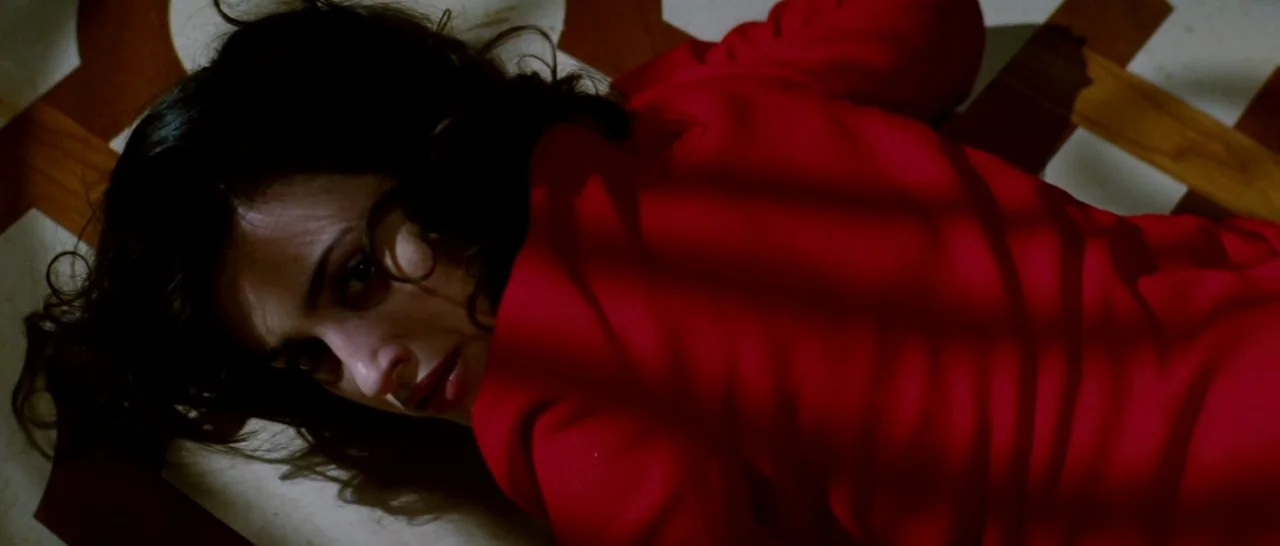 Broken Embraces (2009) movie still: closeup — A dark room features a patterned stone tile floor with light filtered through blinds. A woman wearing…