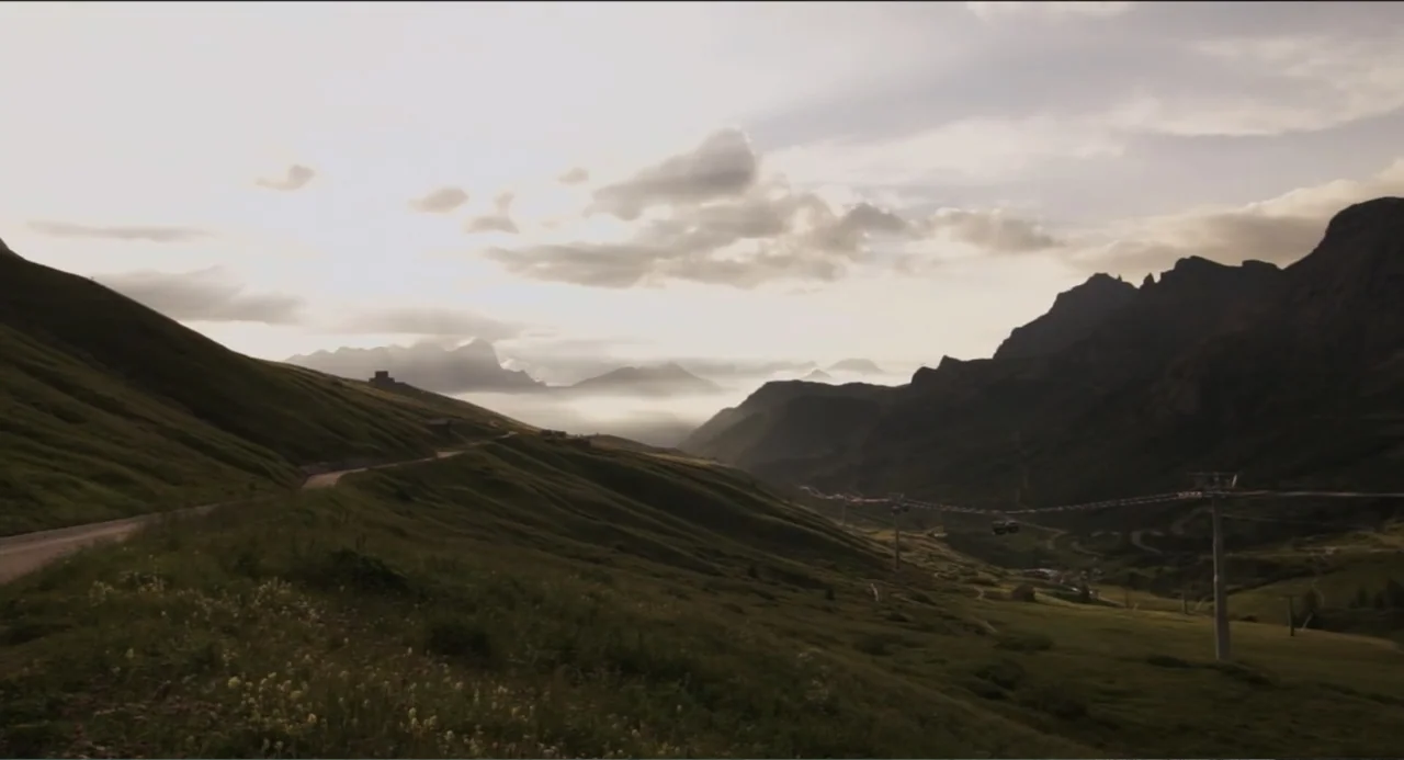 Crooked Trees Gon Give Me Wings (2022) movie still: establishing — A wide mountain valley features rolling grassy slopes and distant jagged peaks.…