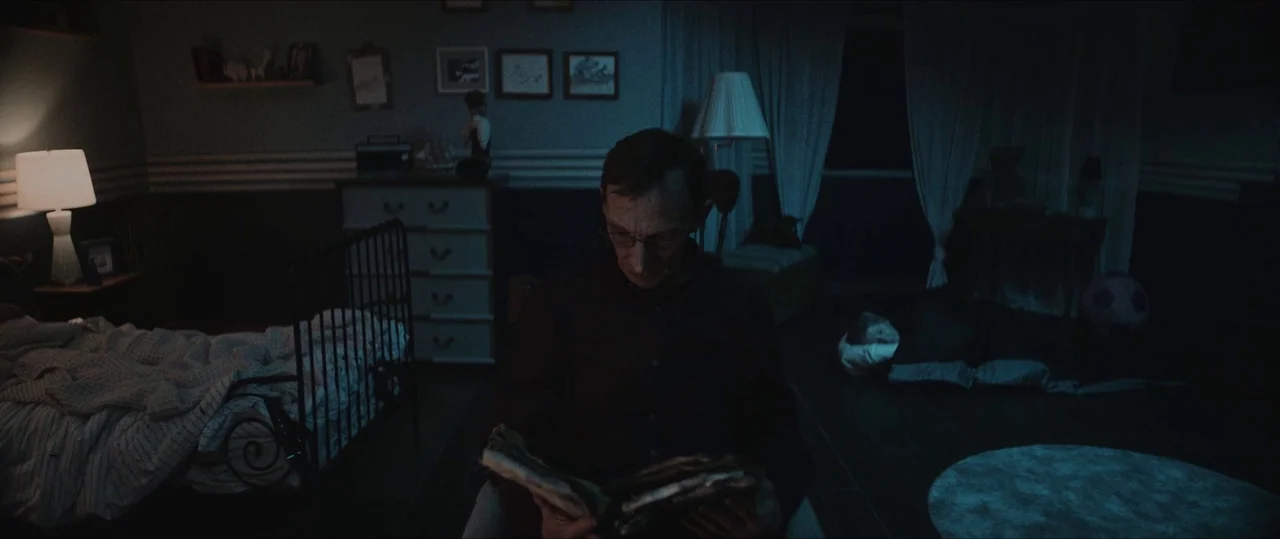 Anything For Jackson (2020) movie still: medium — A dimly lit room with a metal frame bed and a dresser filled with clutter. An older man sits in a…
