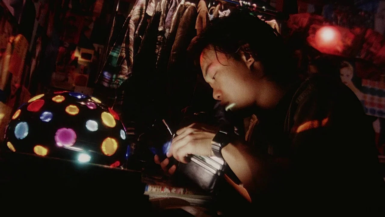 Visible Secret (2001) movie still: medium — A cluttered interior space filled with hanging garments and scattered objects under dim lighting. A…