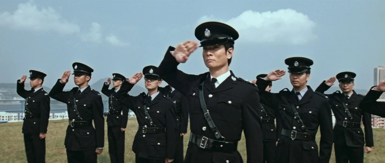 Infernal Affairs (2002) movie still: medium — A row of police officers stands in formation on a grassy rooftop. Each man wears a crisp dark uniform…