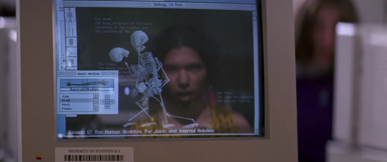 Hackers (1995) movie still: closeup — A 1990s desktop computer monitor displays a biology educational software interface with an anatomy graphic. A…