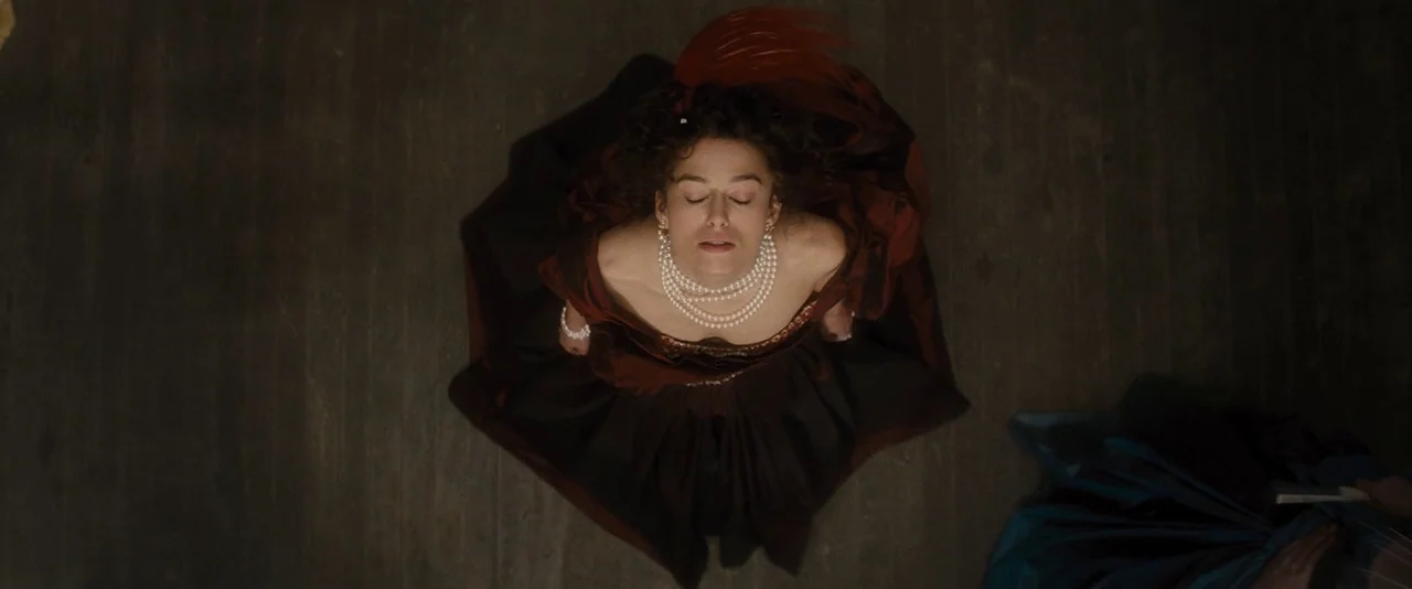 Anna Karenina (2012) movie still: fullbody — An overhead view of a woman in a dark crimson period gown on floor. She stands with her head tilted…