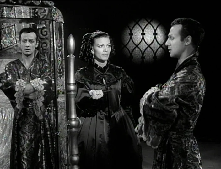 The Devil’s Eye (1960) movie still: medium — A dark, stylized interior with a large ornate mirror frame on the left. A woman holding a small knife…