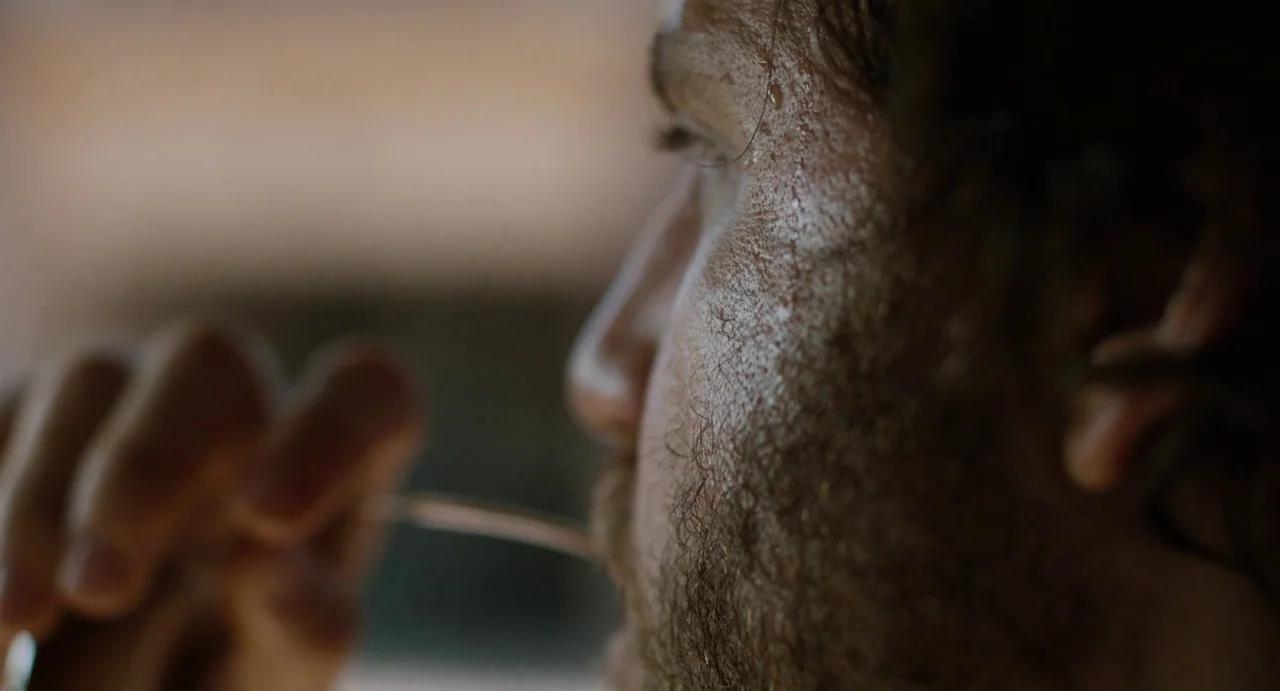 Zero Dark Thirty (2012) movie still: closeup — A close-up view of a man eating in a dimly lit interior environment. The side of his face is visibly…