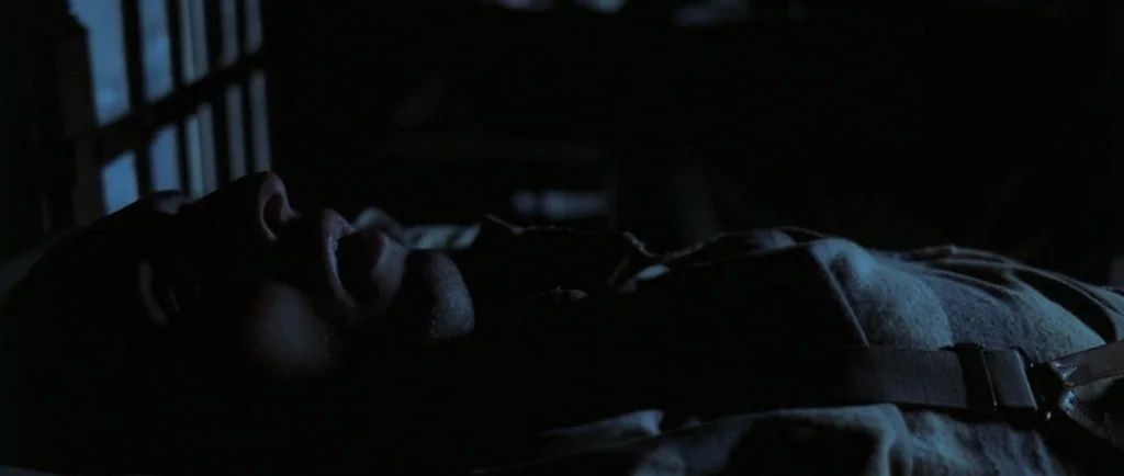O Brother, Where Art Thou? (2000) movie still: closeup — A dark bedroom interior is lit by faint moonlight filtering through a barred window. A man…