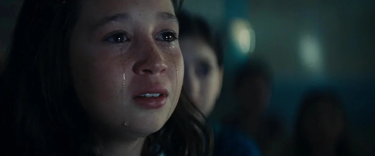 Bridge of Spies (2015) movie still: closeup — A dimly lit indoor space with blurred shapes suggesting other people in the distance. A young girl…