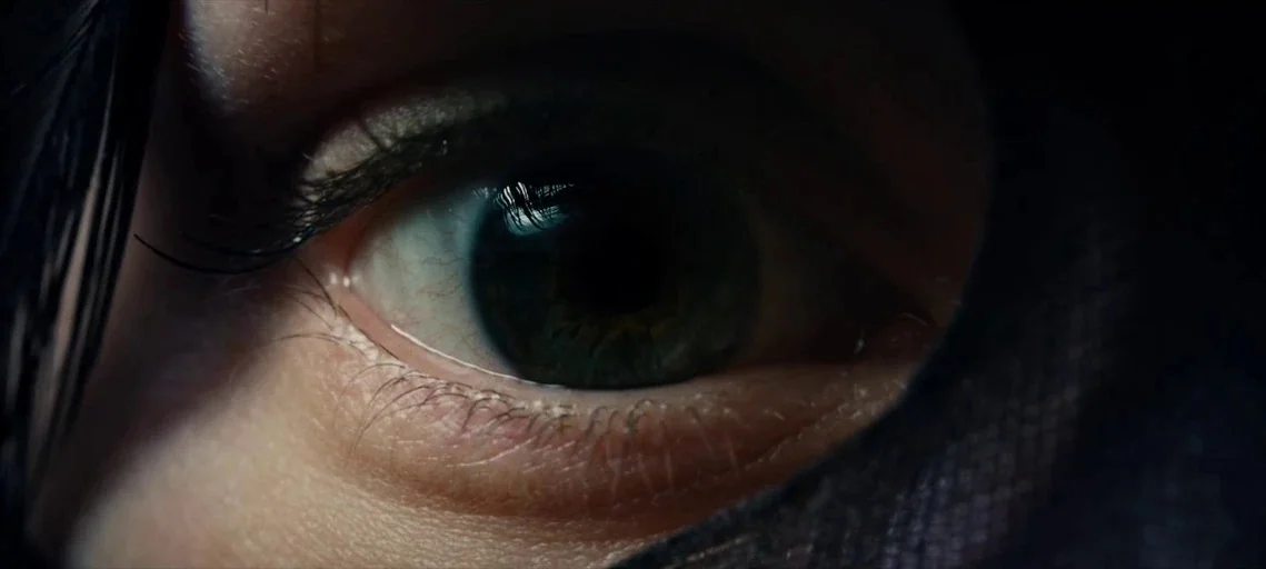 I Origins (2014) movie still: closeup — An extreme close-up focuses on a human eye peering through a dark opening. The iris contains fine details of…