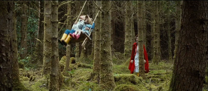 Mister Lonely (2007) movie still: wide — A dense woodland area filled with tall trees covered in thick patches of moss. A child on a hanging swing…