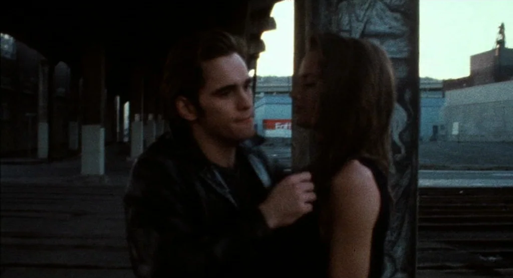 Drugstore Cowboy (1989) movie still: medium — An industrial lot features a concrete overpass and blurred building silhouettes in the background. A…