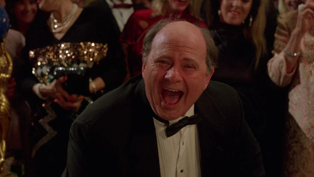 Society (1989) movie still: medium — A crowded formal event features people in evening wear blurred in the background. An elderly man in a black…