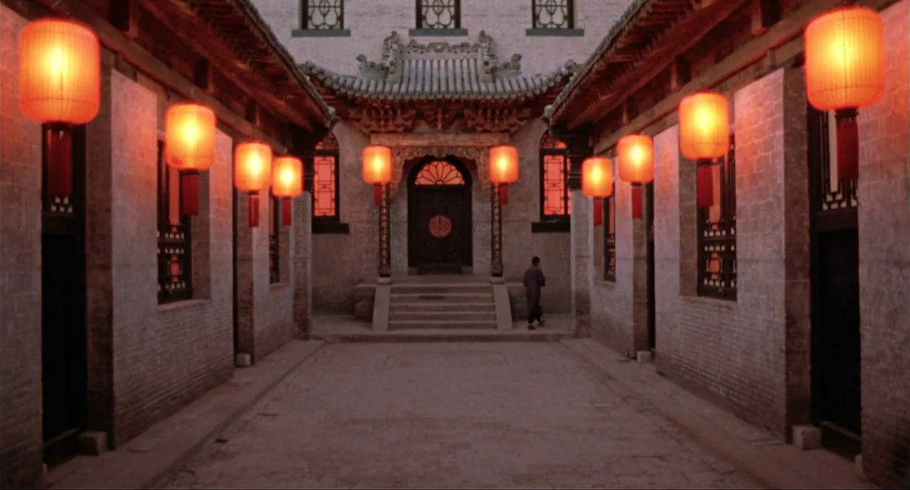 Raise The Red Lantern movie still: wide — A stone courtyard is flanked by symmetrical buildings featuring red hanging paper lanterns. A man walks…